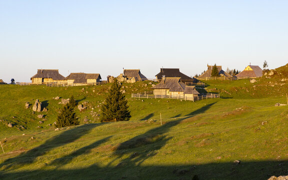 View of traditional wooden huts at Velika Planina on a grassy mountain slope during golden hour in Velika Planina, Kamnik, Slovenia.