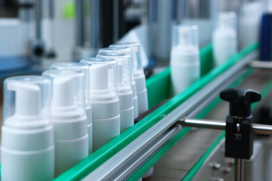 Factory conveyor line: row of white plastic dispenser bottles moves along green production line