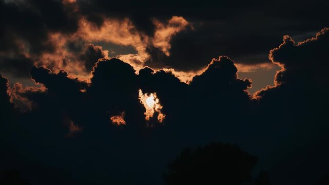 Dramatic sunset over dark clouds with vibrant orange and yellow hues illuminating the sky, showcasing the gradual transition of light and shadow in a natural landscape