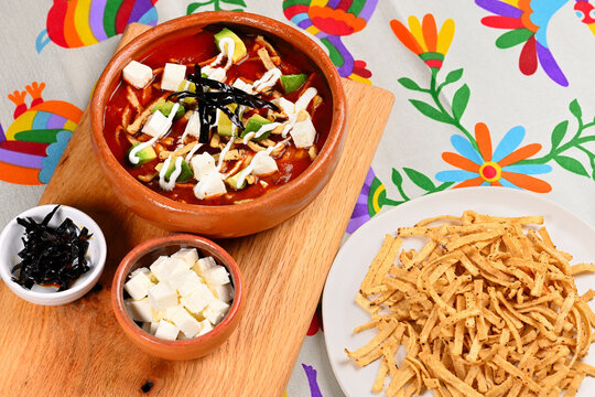High angle view of authentic Mexican sopa de tortilla with toppings on a wooden board and embroidered tablecloth