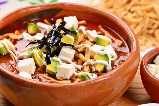 Mexican aztec soup with fried tortilla strips, diced avocado, queso fresco, and dried chili pepper garnish