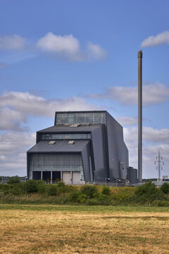 View of a modern biomass energy plant with a tall chimney and industrial architecture set against a blue sky with clouds in Esbjerg, Denmark.