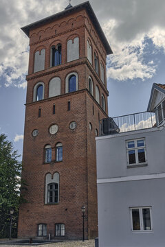 View of the historic Ribe Water Tower with its red brick facade, Romanesque arches, and battlements under a cloudy blue sky in Ribe, Denmark.