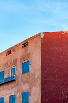 View of a building facade with contrasting red and terracotta walls and bright blue wooden shutters in Essaouira, Marrakesh-Safi, Morocco.