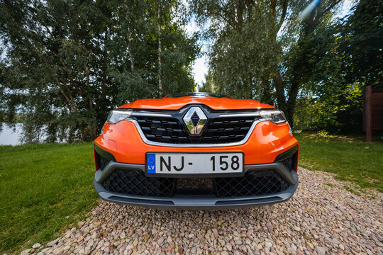 Low angle frontal view of Renault Arkana RS line, bold diamond badge, honeycomb lower grille, vivid orange paint, LED headlamps, LV plate NJ 158, shot outdoors in daylight.