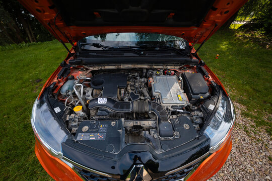 Open hood top down view of Renault Arkana RS Line engine bay, showing turbocharged powertrain, red bodywork, diamond grille badge, battery, air intake, and coolant reservoir.