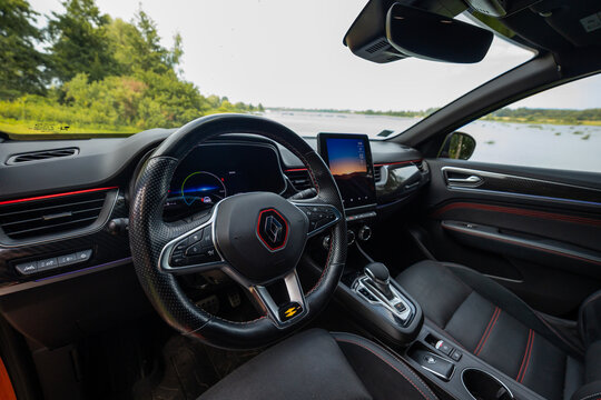 Front seats view shows RS badged flat bottom wheel, digital cluster, portrait touchscreen, red stitching, carbon look trim, water and tree lined shore, early daylight