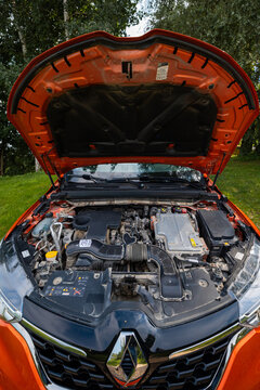 Renault Arkana RS Line outdoors in daylight, open hood shows compact hybrid powertrain, diamond emblem on grille, intake routing, high voltage cables, battery and fuse modules.