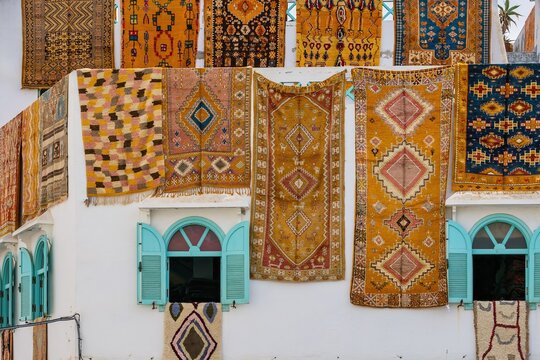 View of traditional Moroccan rugs hanging on the white walls of the historic medina in Asilah, Tangier-Tetouan-Al Hoceima, Morocco.