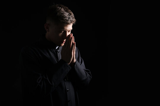 Priest with clasped hands praying on black background. Space for text