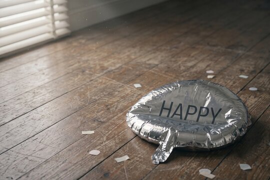 Deflated silver happy balloon on wooden floor with confetti