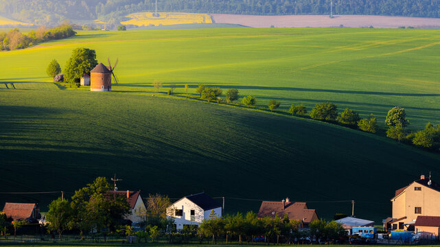 View of a historic windmill standing on a rolling green hill above a small village with houses in Chvalkovice, Hradec Kralove Region, Czechia.