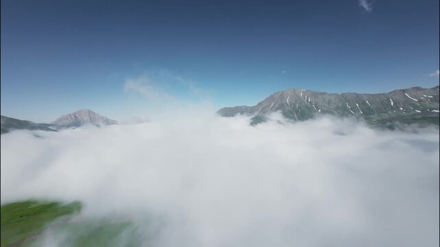 FPV flight through clouds revealing mountains and blue sky in serene landscape