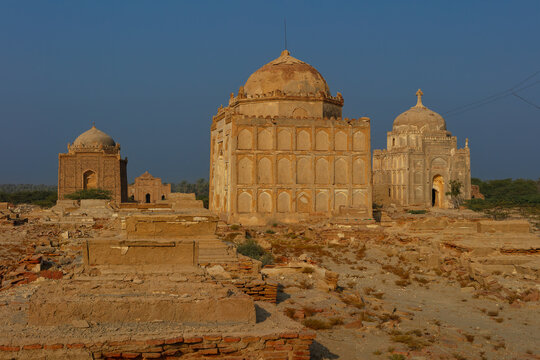 View of the historic Talpur Graveyard featuring ancient domed tombs and weathered stone structures under a clear blue sky in Arror, Sindh, Pakistan.