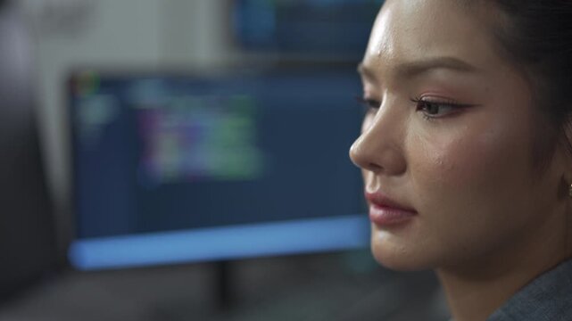 Close up of young female software engineer writing program code on multiple desktop screens in a modern office.
