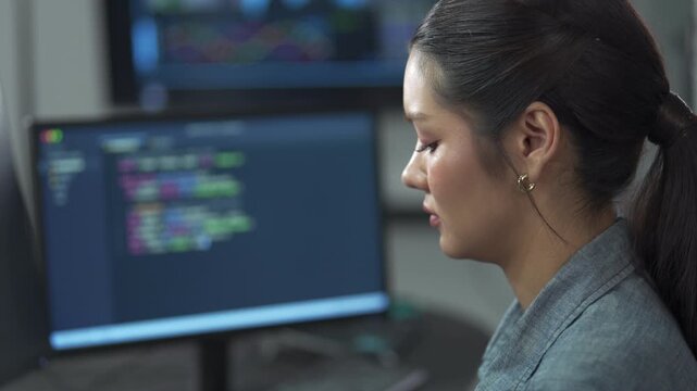 Close up of young female software engineer writing program code on multiple desktop screens in a modern office.
