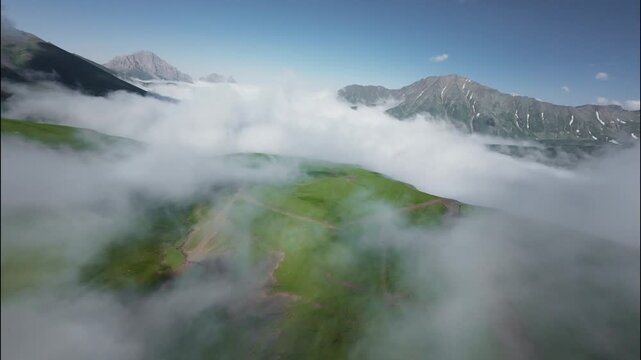 FPV flight through clouds over green hills and mountains under blue sky