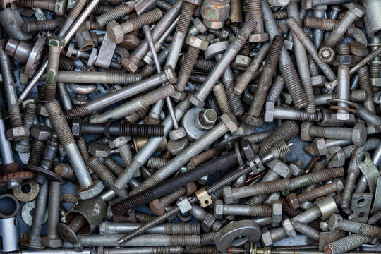 Scattered metallic bolts and screws background. Top down closeup view of messy pile of various old industrial metal bolts screws washers and fasteners