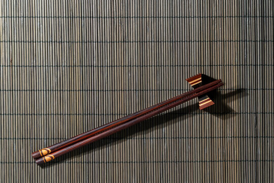 Wooden chopsticks on bamboo mat background, closeup. Top view of traditional wooden chopsticks on holder placed on dark bamboo rolling mat with copy space