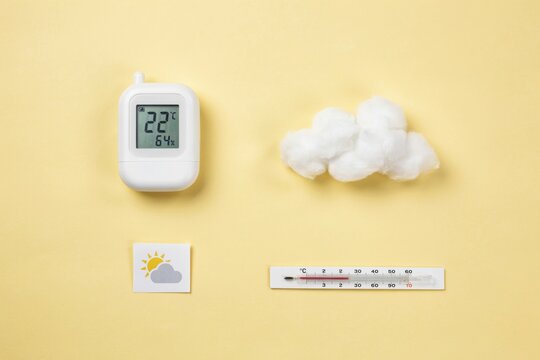 Concept of weather measurement with thermometer, digital hygrometer, and cotton cloud on yellow background
