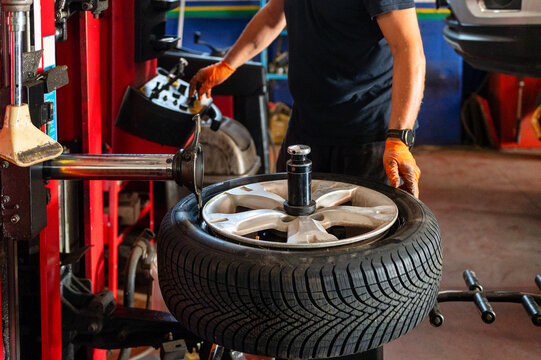 Professional mechanic mounting a car tire on a tire changer machine during automotive maintenance in a repair workshop.