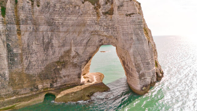 Close aerial view looking through a natural rock arch opening toward the sea