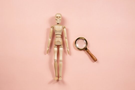 A wooden mannequin and a magnifying glass on a pink background, symbolizing research and analysis