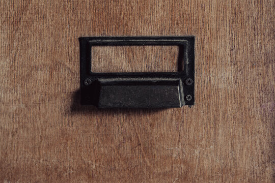 Vintage wooden drawer with empty metal label holder. Closeup of an old wooden library file cabinet drawer with black metal handle and empty index card label slot