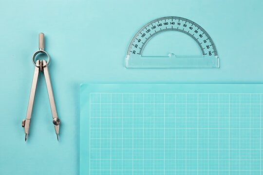 Geometric drawing tools including a compass and protractor on a light blue background with a grid sheet for mathematics and engineering