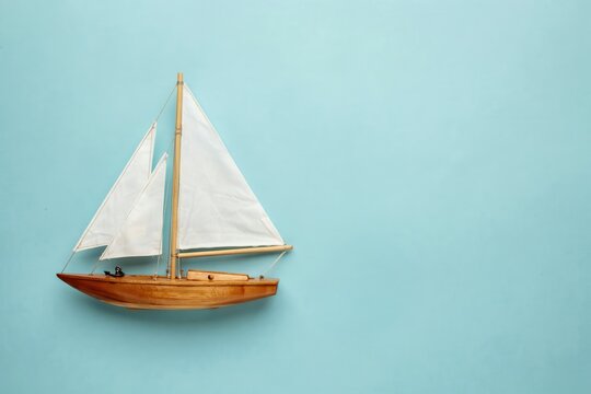 Wooden toy sailboat model on light blue background with copy space