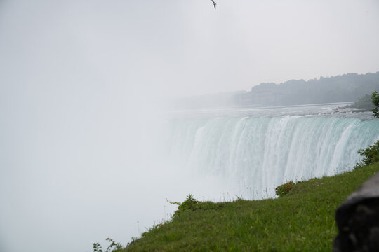 View of Niagara Falls with mist rising from the cascading water and lush green grass in the foreground in Niagara Falls, Ontario, Canada.