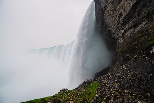 View of the powerful cascading water of Niagara Falls with mist rising against the rocky cliffside in Niagara Falls, Ontario, Canada.