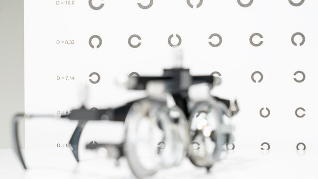 Blurred mechanical part rests against a white target board. Target board displays circular patterns with alphanumeric labels. Soft focus emphasizes the grid's sharp details
