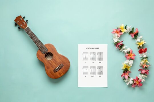 Ukulele with chord chart and tropical flower lei on mint background flat lay