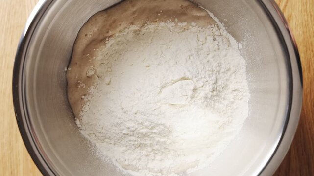 Wheat flour falls into yeast mixture for bread dough. Bread dough combines flour, yeast, water, salt and oil. Bread dough is base for homemade loaves, rolls, baguettes, pizza or sandwich buns.