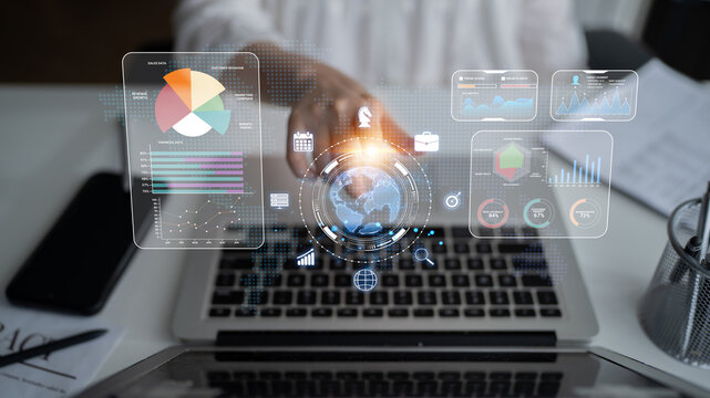 Business professional interacting with futuristic data visualization on laptop screen with digital graphs, charts, and global information display in modern workspace. Sentient.