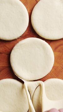Hands peel dough scraps away from cut circles on wooden board. Use dough scraps for biscuits, crackers, pie decor or breadsticks. Dough scraps support zero waste cooking through freezing or baking.