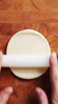 Hands roll pizza dough with plastic pin on board. Pizza dough combines flour, yeast, water, salt and olive oil. Pizza dough forms mini pizzas with cheese, pepperoni, mushrooms, tomatoes or vegetables.