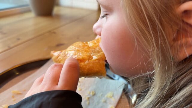Cute child having a sweet snack at a wooden table inside a cozy french bakery close up