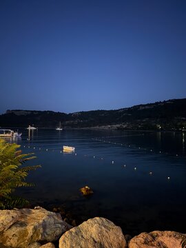 Night view of a calm bay with boats and mountains in the distance near a quiet shoreline