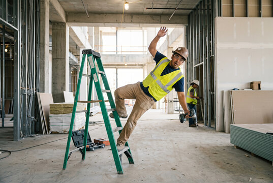 Male construction worker falling backwards off green step ladder at building site