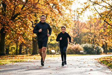 Obraz premium Fit father and young son jogging together in beautiful autumn park