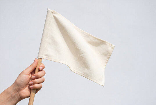 Hand holding a blank off white flag against a light wall