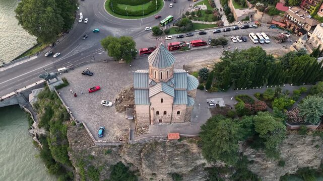 Drone panoramic view of the historic Metekhi Church of the Assumption standing on a cliff above the Kura (Mtkvari) River in Tbilisi, Georgia, with the equestrian statue of King Vakhtang Gorgasali 