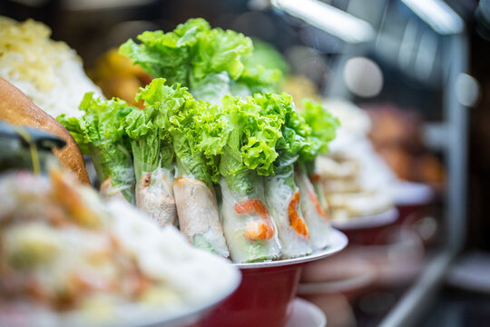 Display of handmade fast food snack plate with rice paper spring rolls with herbs and shrimps at market, popular Vietnamese appetizer selling at street food market, rolls made of lettuce and seafood.