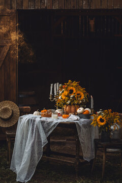 Cozy fall seasonal house decor. Wooden furniture, table setting for thanksgiving dinner with floral centrepiece with sunflowers, pumpkins, candles. Sunset, golden hour. Cozy atmosphere, candlelight