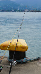 Obraz premium fishing rods resting on a yellow mooring bollard at a harbor pier overlooking the sea and distant mountains 