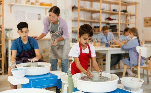 Pleased underage attendees of pottery circle working at throwing-wheel with female instructor