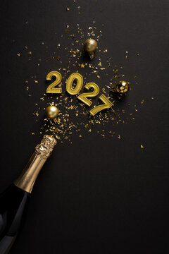 Happy New Year 2027 celebration with gold champagne bottle, confetti and ornaments on black vertical shiny background