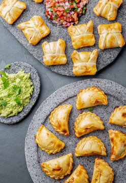 Cocktail empanadas on stone plate with tomato sauce and guacamole .